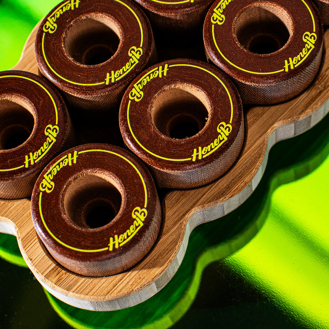 Close-up of several dark brown wooden game discs with yellow 'HereB' branding, arranged on a wavy bamboo tray against a bright neon green reflective background.