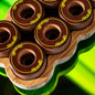 Close-up of several dark brown wooden game discs with yellow 'HereB' branding, arranged on a wavy bamboo tray against a bright neon green reflective background.
