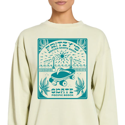 A person wearing a cream-colored crewneck sweatshirt with a teal graphic print on the front that reads 'Fritzy's Roller Skate Shop' and 'Skate Pacific Beach'.